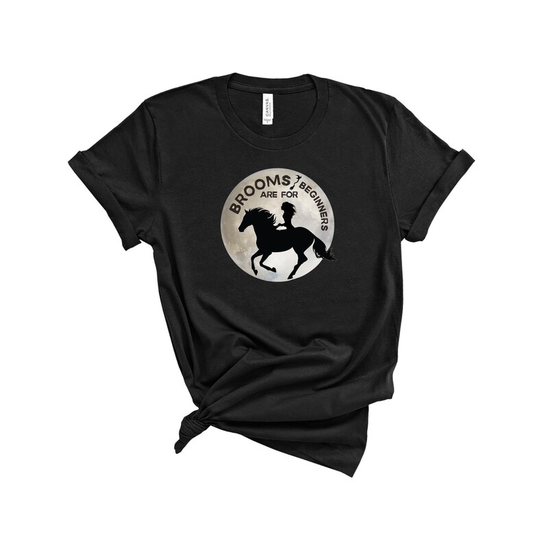 May include: Black t-shirt with a graphic of a silhouette of a woman riding a horse on a moon with the text "Brooms are for beginners".