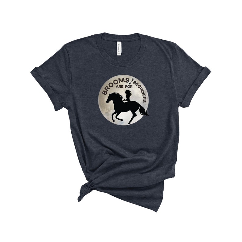May include: A dark blue t-shirt with a graphic of a silhouette of a person riding a horse on a moon with the text "Brooms are for beginners".