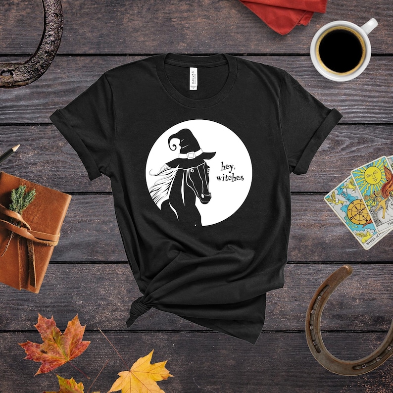 May include: Black t-shirt with a white graphic of a horse wearing a witch's hat and the text "hey, witches".