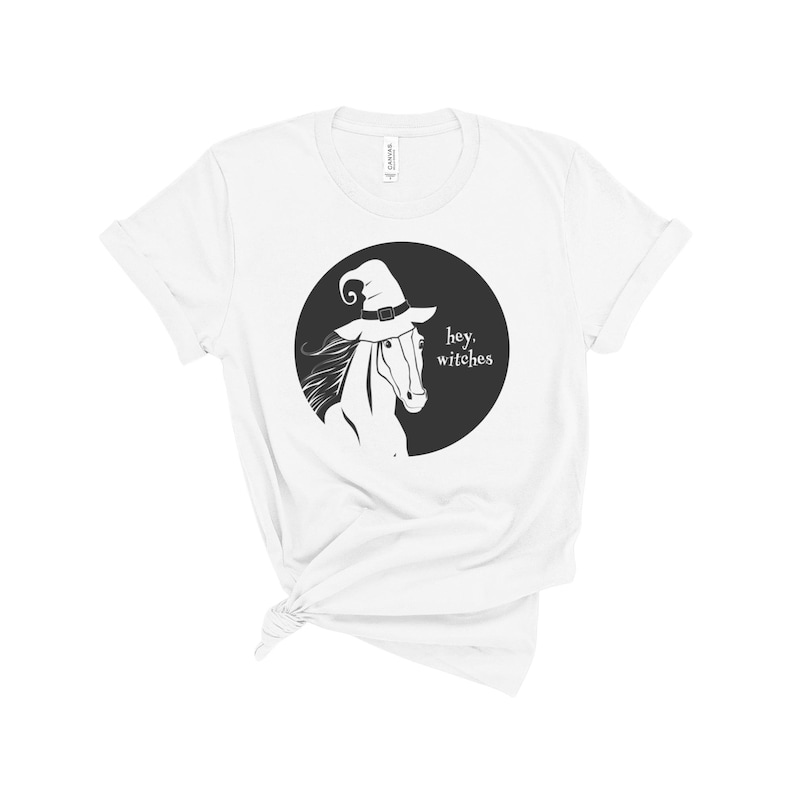 May include: White t-shirt with a black and white illustration of a horse wearing a witch's hat. The text "hey, witches" is printed below the horse.