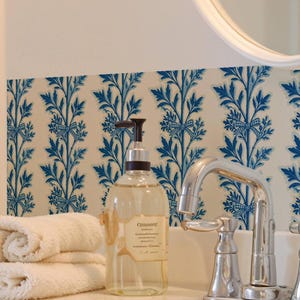Op de afbeelding: Een doorzichtige zeepdispenser van kunststof met een zwarte pomp en een rechthoekig etiket met de tekst "CHELSEA" en "Handwash". De dispenser staat op een wit wastafelblad naast twee opgevouwen witte handdoeken en een chromen kraan.