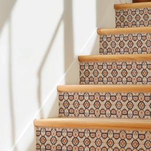 May include: Wooden staircase with decorative risers. The risers feature a repeating pattern of beige, orange, and navy blue floral designs. The steps are made of light-colored wood.
