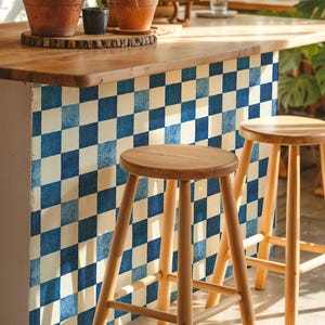 May include: A kitchen island with a wooden worktop and a blue and white chequered pattern on the side. Two wooden stools are in front of the island. Potted plants sit on the worktop.