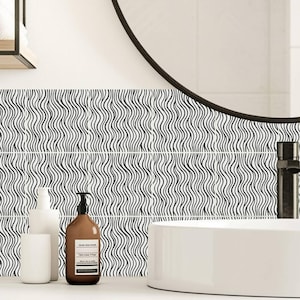 May include: Bathroom decor featuring a white ceramic sink, a round black mirror, and a wall with black and white wavy pattern tiles. Soap dispensers and a cup are on the countertop. The overall aesthetic is modern and minimalist.