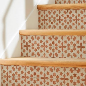 May include: A staircase featuring light-coloured wooden treads and risers decorated with square tiles. The tiles have a white background and a repeating terracotta-coloured star pattern. The stairs are set against a plain white wall.