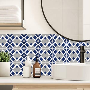 Puede incluir: Decoración de baño con un protector contra salpicaduras de azulejos geométricos con un patrón repetitivo de diamantes azules, blancos y grises. Un lavabo blanco, un espejo y un mueble de madera completan el diseño moderno.