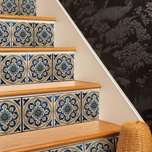 Könnte beinhalten: Holztreppe mit dekorativen Fliesen mit blau-gelbem Blumenmuster. Die Fliesen sind an den Setzstufen der Stufen angebracht. Ein geflochtener Korb steht am Fuß der Treppe, und eine dunkle Blumentapete ist sichtbar.