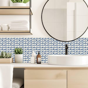 May include: A bathroom wall featuring a repeating pattern of blue and white wave-themed tiles. The tiles are arranged in a horizontal backsplash design behind a white sink, a black faucet, and a round mirror with a thin black frame.