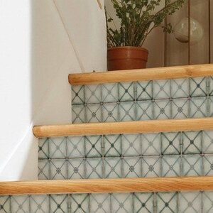 May include: Staircase with light blue and white patterned tiles and wooden handrails. A potted plant and a decorative lantern are visible on the landing. The tiles have a geometric design.