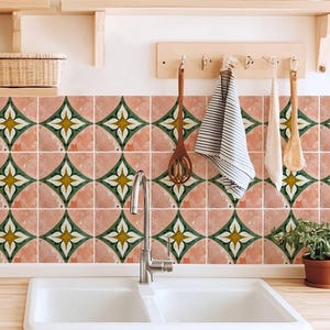 Może przedstawiać: Kuchnia z dekoracyjną, kafelkową ścianą. Płytki mają różowe tło i zielono-żółty kwiatowy wzór. Kuchnia posiada również biały podwójny zlew, drewniane półki i rośliny doniczkowe.