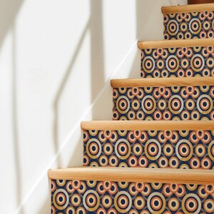 May include: A staircase with wooden treads and risers covered in a repeating geometric pattern of concentric circles in shades of navy blue, burnt orange, cream, and mustard yellow, creating a vibrant and rhythmic visual effect on each step.