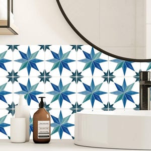 Puede incluir: Decoración de baño con encimera blanca, lavabo y azulejos de pared con estampado de estrellas azules y turquesas. También se ven un espejo redondo negro y un mueble de madera. Hay botellas blancas y marrones en la encimera.