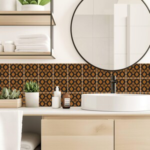 May include: A set of square wall tiles featuring a repeating black and burnt orange floral pattern. The tiles are arranged in a grid on the wall behind a white vessel sink, a round mirror, and a light wood vanity with open shelving.