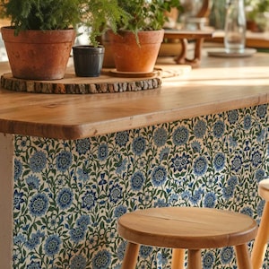 May include: A kitchen island featuring a blue and green floral pattern on the front panel, topped with a light wood counter. Two terracotta pots containing green plants sit on a circular wooden base on the counter, next to a wooden stool.
