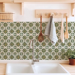 May include: A kitchen interior with a white double sink and chrome tap, complemented by a backsplash of green and yellow patterned tiles. Wooden shelves display plants and utensils, creating a bright and welcoming atmosphere.