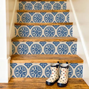 May include: A staircase with natural wood treads and risers decorated with a blue and white circular floral pattern. A pair of cream-coloured rubber boots with small multicoloured polka dots sits on the second step from the bottom of the stairs.