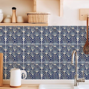 Puede incluir: Un conjunto de azulejos cuadrados con un patrón repetitivo en forma de abanico en azul oscuro y crema. Los azulejos están dispuestos en una cuadrícula en el salpicadero de la cocina, creando un diseño geométrico continuo tras el fregadero.