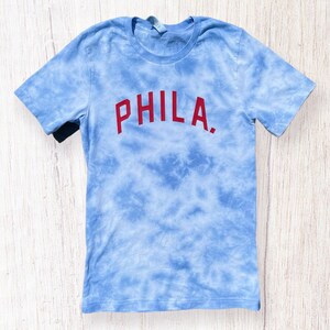 May include: A blue tie-dye t-shirt with the word "PHILA." printed in red.