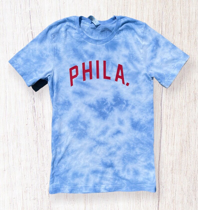 May include: A blue tie-dye t-shirt with the word "PHILA." printed in red.