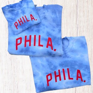 May include: Three blue tie-dye sweatshirts with the word "PHILA." printed in red on the front.