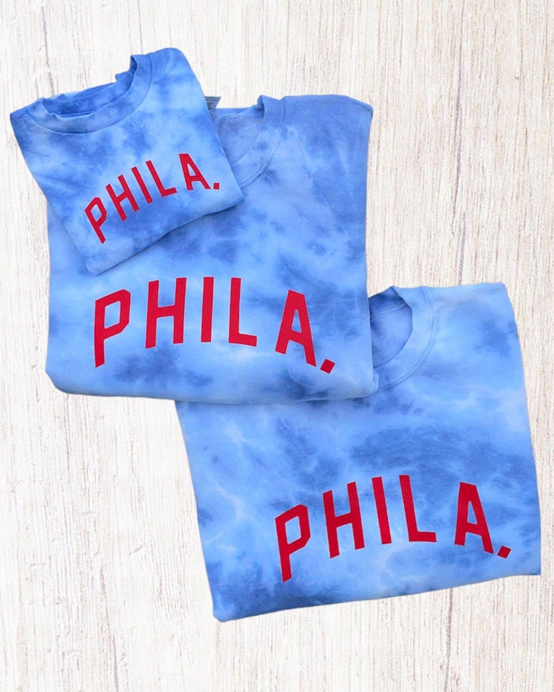 May include: Three blue tie-dye sweatshirts with the word "PHILA." printed in red on the front.