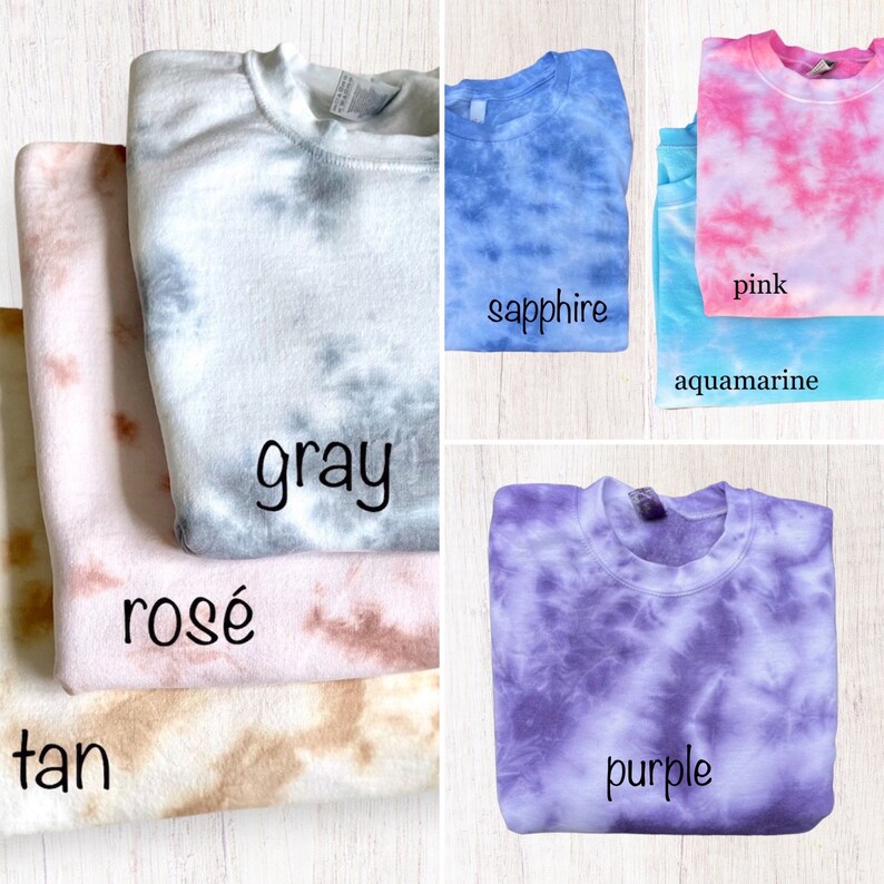 Pu&ograve; includere: Un mucchio di felpe tie-dye in vari colori, tra cui beige, rosa, grigio, acquamarina, rosa, zaffiro e viola. Le felpe sono piegate e disposte in fila.