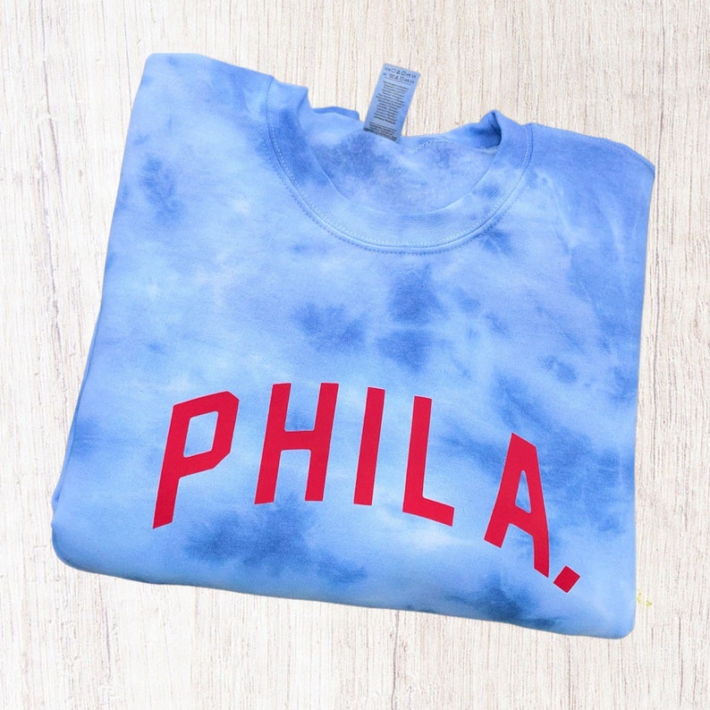 May include: A blue tie-dye sweatshirt with the word "PHILA" in red lettering.