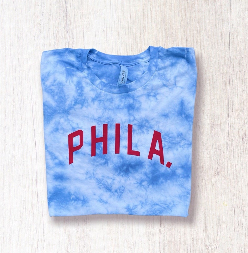 May include: A blue tie-dye t-shirt with the word "PHILA." printed in red on the front.