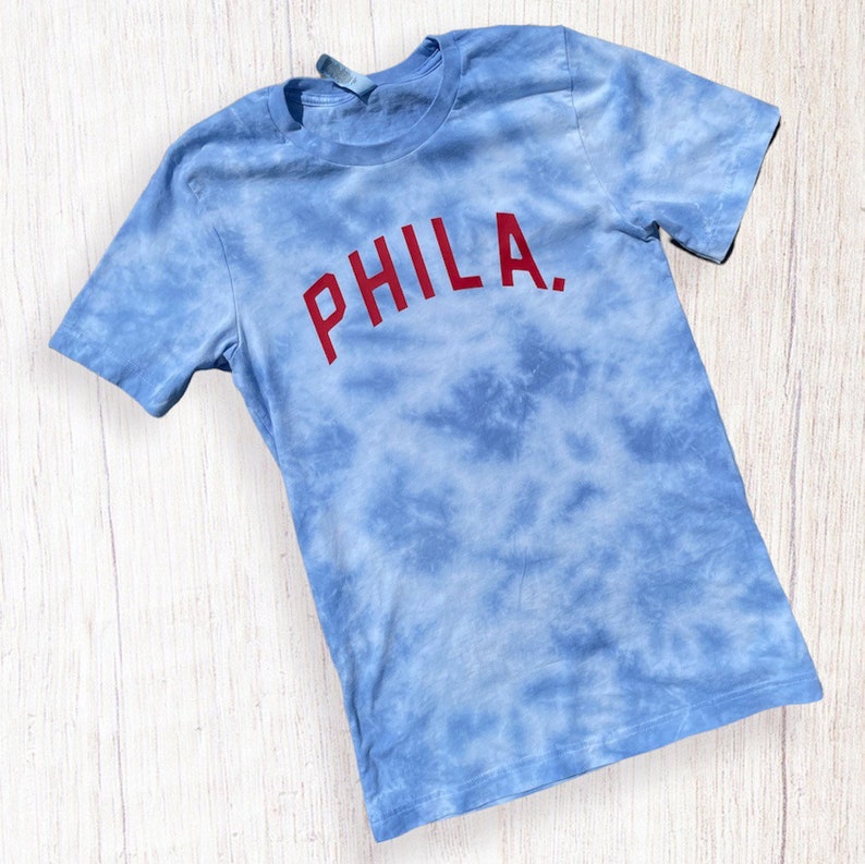 May include: A blue tie-dye t-shirt with the word "PHILA." in red lettering.