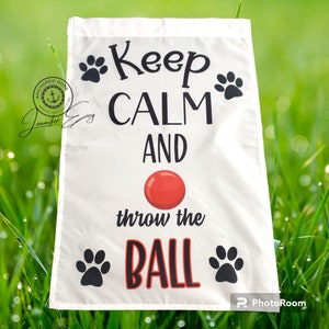 May include: White garden flag with black paw prints and the text "Keep Calm and throw the BALL" in black and red lettering. A red ball is pictured above the text "throw the".