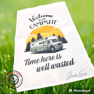 May include: White camping sign with a graphic of a motorhome in front of a sunset and trees. The text reads "Welcome to our CAMPSITE Time here is well wasted".