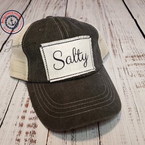 May include: A black and white trucker hat with a white patch that says "Salty" in black cursive script.