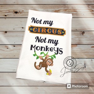 May include: White kitchen towel with the text "Not my circus, Not my monkeys" in black lettering. A cartoon monkey with a banana is hanging from a vine. The text "Anchored Hope Christian Clothing" is in a circle with an anchor in the center.