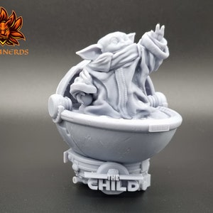 May include: A gray 3D printed figurine of a character from the Star Wars series, The Mandalorian. The character is sitting in a round pod with the text "The Child" on the base.