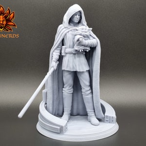 Puede incluir: Una figura impresa en 3D de color gris de un personaje de la franquicia Star Wars, sosteniendo una peque&ntilde;a figura en sus brazos. El personaje lleva una t&uacute;nica con capucha y sostiene un sable de luz. La figura est&aacute; de pie sobre una base circular.