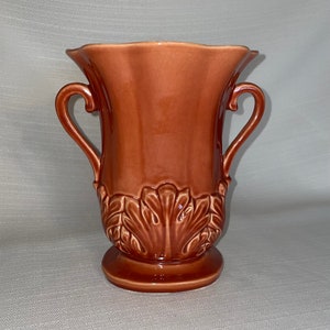 May include: A brown ceramic vase with two handles and a leaf design. The vase has a scalloped rim and a rounded base.