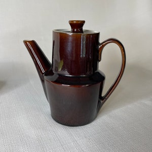 May include: A brown ceramic teapot with a white lid and a brown handle. The teapot has a rounded body and a spout on the side.