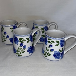 May include: Set of four white ceramic mugs with blue and green floral designs. Each mug has a handle.