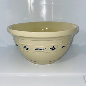 May include: A cream-colored ceramic mixing bowl with a blue floral design around the exterior. The bowl has a rounded shape and a wide rim. The blue design consists of floral patterns and curved lines. This vintage bowl is perfect for baking.