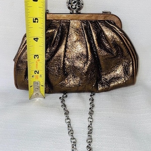 Pode incluir: Uma clutch bronze com acabamento texturizado e al&ccedil;a de corrente prateada. A clutch tem aproximadamente 15 cm de altura. Possui um fecho decorativo de bola prateada. Um acess&oacute;rio elegante para ocasi&otilde;es especiais.