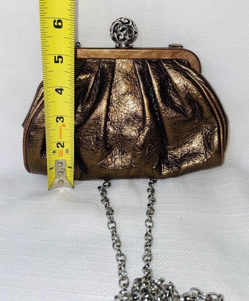 Pode incluir: Uma clutch bronze com acabamento texturizado e al&ccedil;a de corrente prateada. A clutch tem aproximadamente 15 cm de altura. Possui um fecho decorativo de bola prateada. Um acess&oacute;rio elegante para ocasi&otilde;es especiais.