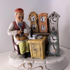 May include: A porcelain figurine of a clockmaker working on a clock. He is sitting in a chair with tools and parts around him. There are four clocks on the wall behind him, each with a different design.