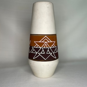 May include: White ceramic vase with a geometric pattern in brown, orange, and white. The pattern features triangles and lines.