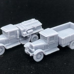 May include: Two miniature grey plastic truck models. One vehicle features a flatbed cargo area with side panels, while the other is equipped with a cylindrical tank body. Both models display detailed cabs, fenders, and wheels in a monochromatic finish.