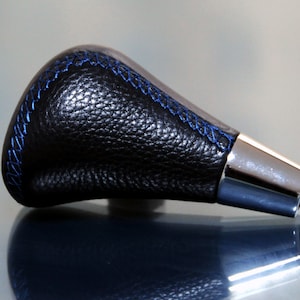 Könnte beinhalten: Schwarzer Leder-Schalthebelknauf mit blauen Nähten und einem verchromten Sockel.