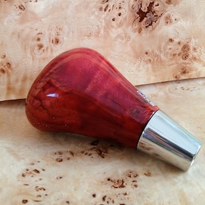 May include: A red wood gear shift knob with a silver metal base. The knob is made of wood with a red stain and a glossy finish.