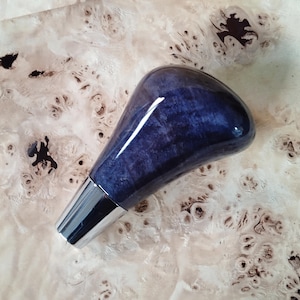 Puede incluir: Un tapón de botella azul y plateado con un acabado brillante. La parte superior es azul oscuro con un efecto veteado, mientras que la base es plateada. El tapón está diseñado para encajar en una botella.