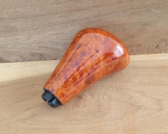 May include: A wooden car gear shift knob with a glossy finish. The knob is a warm, reddish-brown color with a unique wood grain pattern. The base of the knob is black.