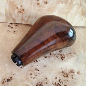 May include: A dark brown wooden gear shift knob with a shiny finish. The knob has a metal ring at the bottom.
