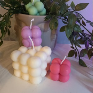 May include: Three bubble candles in different colours: green, purple and pink. The candles are stacked on top of each other, with the green candle on top.